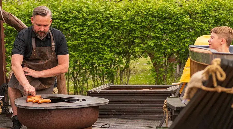 Ein Mann grillt Würstchen auf einem Holzkohlegrill, während ein Junge zuschaut.